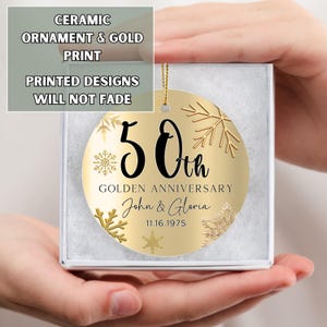 May include: Gold ceramic ornament with a gold snowflake design and the text "50th Golden Anniversary John & Gloria 11.16.1975"