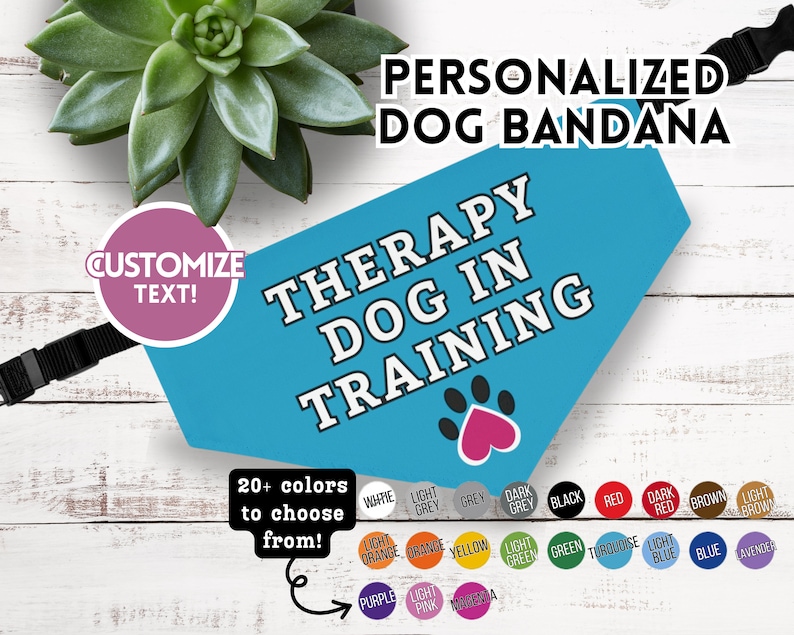 K&ouml;nnte beinhalten: T&uuml;rkisblaues, personalisiertes Hundehalstuch mit dem wei&szlig;en Text "THERAPY DOG IN TRAINING". Es zeigt einen rosa Pfotenabdruck und einen schwarzen, verstellbaren Riemen. &Uuml;ber 20 Farben stehen zur Auswahl.