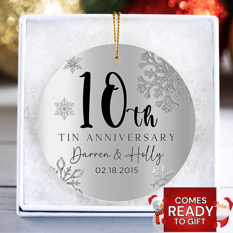 May include: A silver and white round Christmas ornament with a snowflake design. The ornament says "10th Tin Anniversary Darren & Holly 02.18.2015".