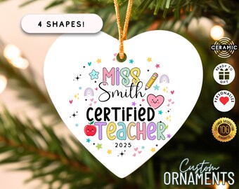 May include: A white heart-shaped ceramic ornament with the text "Miss Smith Certified Teacher 2025" in colorful letters. The ornament has a gold string for hanging and includes a pencil, apple, and heart graphic.