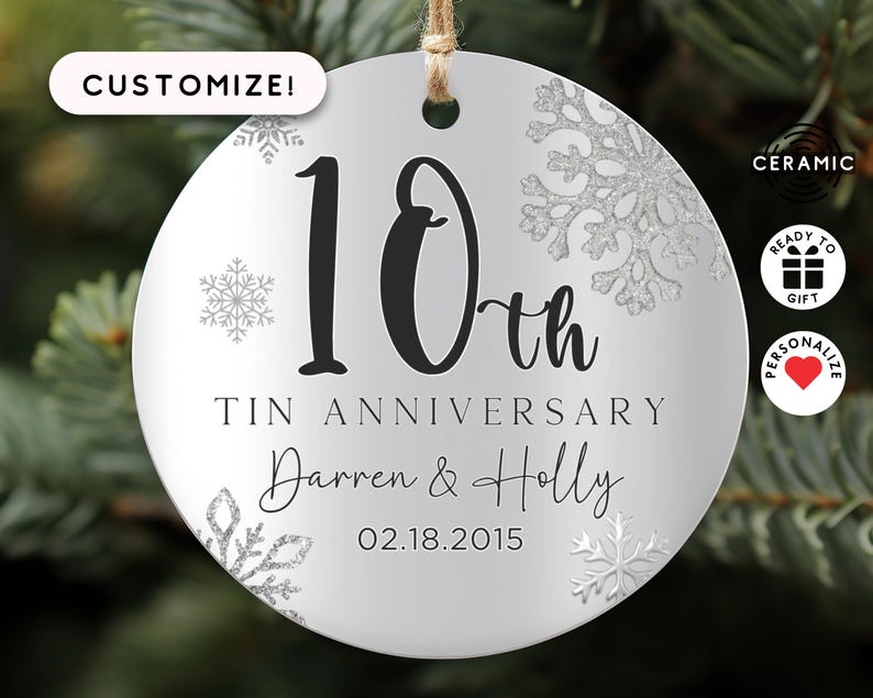 May include: A white ceramic ornament with a silver glitter snowflake design. The ornament features the text "10th Tin Anniversary Darren & Holly 02.18.2015".
