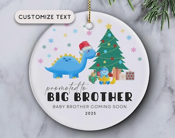May include: Round Christmas ornament with a blue dinosaur wearing a Santa hat, a Christmas tree, and the text "promoted to BIG BROTHER" and "BABY BROTHER COMING SOON 2025". The ornament has a gold string for hanging.