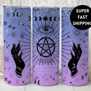 May include: A purple and blue tumbler with a celestial design. The design includes a pentagram, an eye, hands, and stars. The tumbler has the name "Amber" on it.