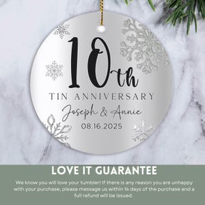 May include: A silver round ornament with a white background and silver glitter snowflakes. The ornament says "10th Tin Anniversary Joseph & Annie 08.16.2025".