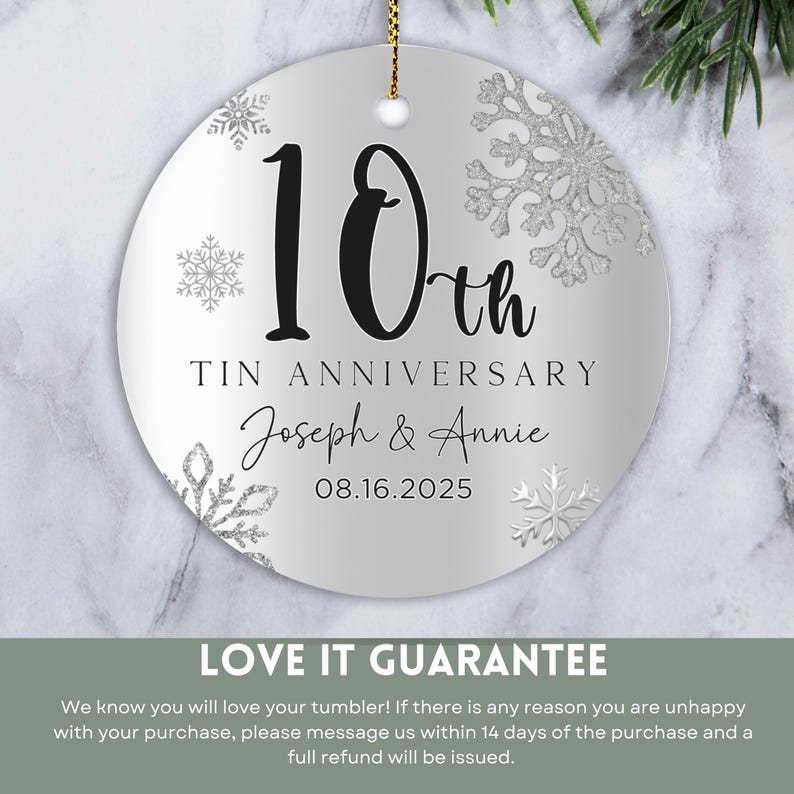 May include: A silver round ornament with a white background and silver glitter snowflakes. The ornament says "10th Tin Anniversary Joseph & Annie 08.16.2025".