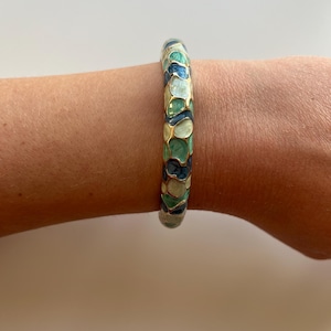 Könnte beinhalten: Ein goldenes Armreif-Armband mit einem Mosaikdesign aus blauem, grünem und weißem Emaille.