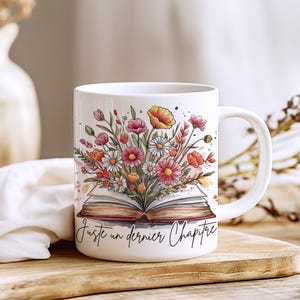Peut inclure: Mug en céramique blanche avec une illustration à l'aquarelle d'un livre ouvert et de fleurs colorées. La tasse a une anse incurvée et le texte "Juste un dernier Chapitre" en écriture noire.