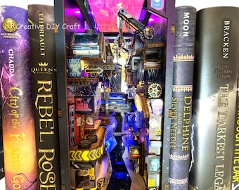 May include: A detailed, illuminated diorama of a futuristic cityscape, nestled between hardcover books. The miniature scene features neon signs, mechanical elements, and the text "Creative DIY Craft". The diorama is lit with blue and purple lights.