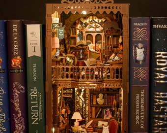May include: A wooden miniature model of a library with a cat sitting on a desk, surrounded by books. The model is displayed on a bookshelf with other books, including "The Return" by Disney Hyperion, "Escape from the Lost City" by Disney Hyperion, and "Royal Bastards" by Hyperion.