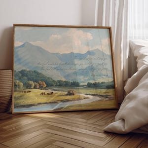 May include: Framed landscape art print featuring a serene mountain scene with a river and grazing animals. The artwork has a vintage aesthetic with soft colors and a wooden frame. Text is visible in the upper right corner.