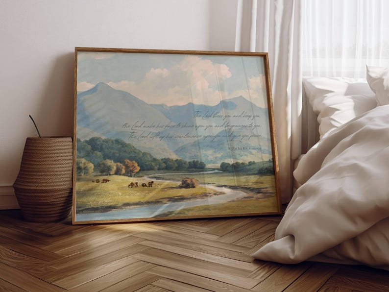 May include: Framed landscape art print featuring a serene mountain scene with a river and grazing animals. The artwork has a vintage aesthetic with soft colors and a wooden frame. Text is visible in the upper right corner.