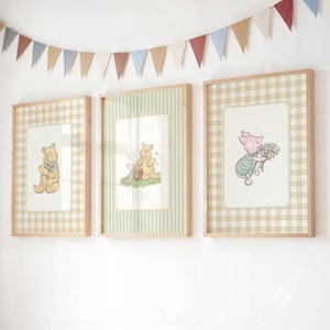 May include: Three framed Winnie the Pooh art prints. Each print features a different character illustration on a patterned background. The frames are light wood, and a colourful banner hangs above the prints.