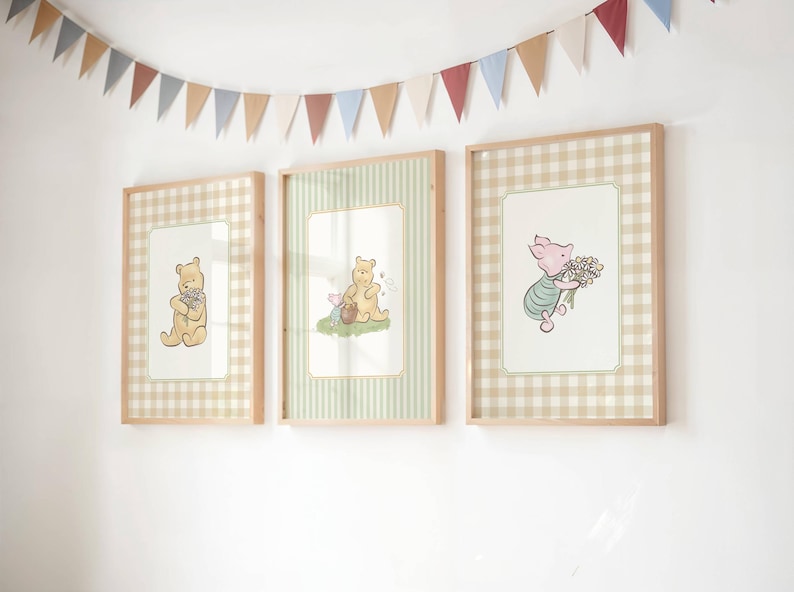 May include: Three framed Winnie the Pooh art prints. Each print features a different character illustration on a patterned background. The frames are light wood, and a colourful banner hangs above the prints.