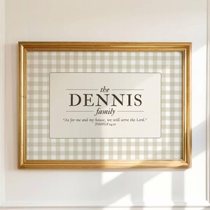 May include: A framed family sign with a gold-colored frame. The sign features the text "the DENNIS family" in a serif font, along with a quote from Joshua 24:15. The background is a beige and white gingham pattern.