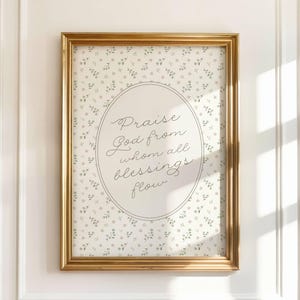 Puede incluir: Un marco dorado enmarca una impresión con un fondo floral y un óvalo con la inscripción "Praise God from whom all blessings flow" en escritura elegante.