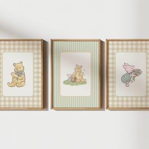 May include: Three framed prints featuring Winnie the Pooh characters. Each print has a light brown wooden frame. The first print shows Pooh holding flowers, the second shows Pooh and Piglet, and the third shows Piglet holding flowers. The background has a gingham or striped pattern.