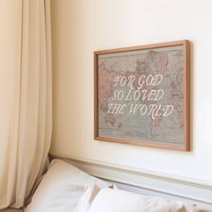 May include: A framed world map print with the text "FOR GOD SO LOVED THE WORLD" in white script. The map has a vintage aesthetic with muted colors and is displayed on a white wall.