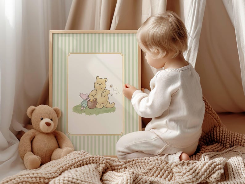 May include: A framed illustration of Winnie the Pooh and Piglet, set against a light green and white striped backdrop. A soft teddy bear rests on a beige blanket. A child in white clothing is looking at the framed picture.