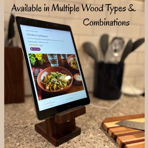 May include: A dark wood tablet stand holding a tablet displaying a Chicken Carbonara recipe. The stand is square-based with a horizontal support. Text at the top reads "Available in Multiple Wood Types & Combinations."