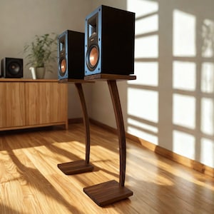 May include: Two black bookshelf speakers with prominent copper-colored circular drivers, each mounted on a dark brown wooden stand featuring a single curved vertical support and a flat rectangular base, positioned on a light-colored wooden floor.