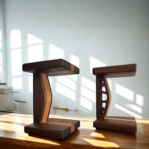May include: Two dark brown wooden speaker stands with a C-shaped profile. The left stand features a solid vertical support, while the right stand has a cutout design. Both stands have a flat base and top platform with a lighter wood accent strip.