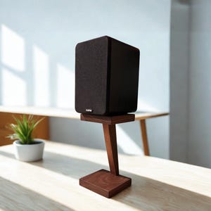 May include: A black rectangular speaker with a fabric grille and the brand name SVS printed in white, resting on a dark brown wooden stand featuring a square base, a single angled support pillar, and a flat top platform for the speaker unit.