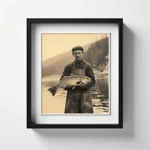 Può includere: Una fotografia in bianco e nero di un uomo che tiene un grosso pesce in un fiume. Indossa un berretto e una tuta. La foto è incorniciata in una cornice nera.