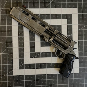 Könnte beinhalten: Ein metallisch grauer Revolver mit schwarzem Griff. Die Waffe verfügt über eine Trommel, einen Abzug und eine obere Schiene. Das Design umfasst ein rotes Visier und verschiedene mechanische Details, die eine futuristische oder Science-Fiction-Ästhetik suggerieren.