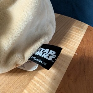 Puede incluir: Un juguete de peluche blanco con una etiqueta negra que dice "STAR WARS" y "& Lucasfilm Ltd."