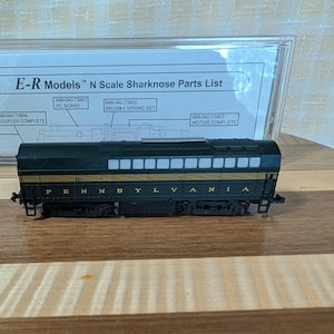 May include: A model train car with the word "PENNSYLVANIA" printed on the side. The car is dark green with gold trim and black wheels. The text "E-R Models N Scale Sharknose Parts List" is visible in the background.