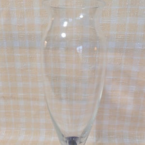 May include: A clear glass vase with a flared top and a blue base. The vase has a slender, elongated shape, perfect for displaying flowers or decorative branches. The blue base adds a pop of color to the otherwise transparent design.