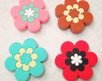 Op de afbeelding: Vier bloemvormige onderzetters of decoratieve items van siliconen. Linksboven: roze, mintgroen en wit. Rechtsboven: bruin, crème en oranje. Linksonder: talingblauw, lichtgeel en lichtblauw. Rechtsonder: rood, zwart en wit.