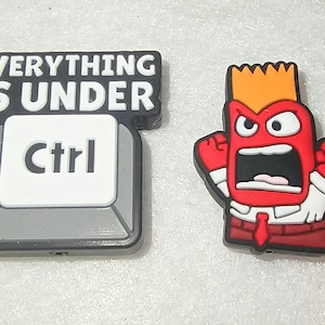 May include: Two colorful rubber charms. One is a black and gray Ctrl key with the text "EVERYTHING IS UNDER Ctrl". The other is a red cartoon character with orange hair, an angry expression, and a white shirt.