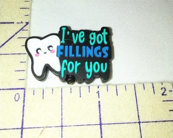 Op de afbeelding: Een zwart-witte bedel met de tekst "I've got FILLINGS for you". De bedel toont een cartoon tand met een lachend gezicht. De tekst is in teal en blauw.