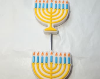 Op de afbeelding: Twee identieke bedels in de vorm van een menora met een gele basis en negen lichtblauwe kaarsen met oranje vlammen. De bedels zijn verticaal uitgelijnd en geregen op een dunne, rechte, zilverkleurige metalen staaf of pin.
