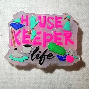 May include: A pink and white House Keeper Life charm with cleaning supplies and text. The word "HOUSEKEEPER" is in bright pink, and "life" is in black script. Cleaning tools include a mop, gloves, and spray bottles.