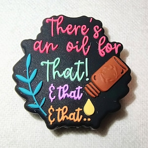May include: A black, irregularly shaped charm with the text "There's an oil for that! & that & that.." in pink, green, purple, and orange. A brown essential oil bottle and a yellow oil drop are also featured.