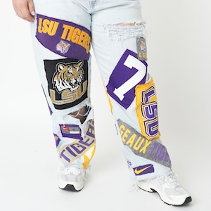 Op de afbeelding: Lichtblauwe spijkerbroek met meerdere patches met het LSU Tigers logo, de woorden "LSU Tigers" en het nummer "7".