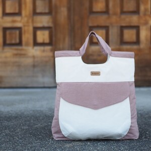 May include: A large, pink and white canvas tote bag with a brown leather label that says "Buddhalife".