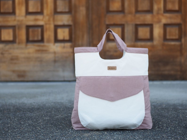 May include: A large, pink and white canvas tote bag with a brown leather label that says "Buddhalife".