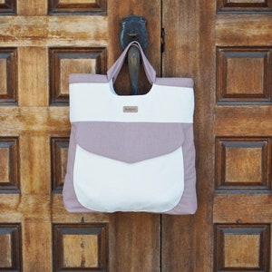 May include: A white and light pink tote bag with a pocket on the front. The bag has a brown leather tag with the word "Wildfolk" on it.