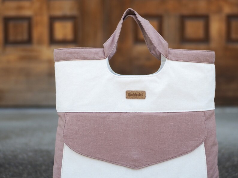 May include: A white and pink canvas tote bag with a brown leather label that says "remarkable".