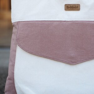 May include: A white canvas tote bag with a large pink pocket and a brown leather label that says "Madeofalab".