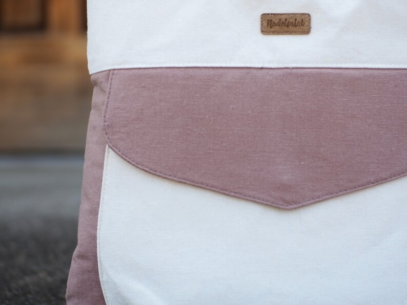 May include: A white canvas tote bag with a large pink pocket and a brown leather label that says "Madeofalab".