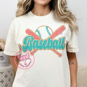 May include: A white t-shirt with a teal and gold glitter design of crossed baseball bats and a baseball with the word "Baseball" in teal glitter letters.