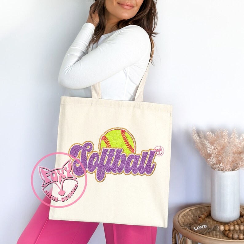 May include: A white canvas tote bag with a purple and gold glitter design that says "Softball" with a yellow softball graphic.