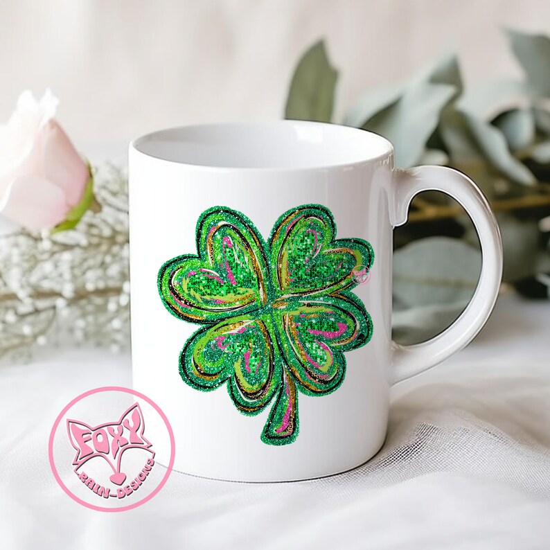 Peut inclure: Une tasse en c&eacute;ramique blanche avec un motif de tr&egrave;fle &agrave; quatre feuilles vert. Le tr&egrave;fle est soulign&eacute; d'or et a un effet de paillettes roses.