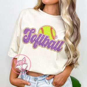 May include: A white t-shirt with a purple and gold glitter design that says "Softball" with a yellow softball graphic.