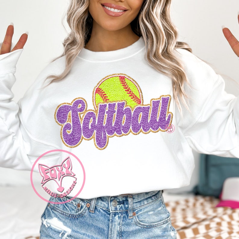May include: White sweatshirt with a purple and gold glitter design that says "Softball" with a yellow softball graphic.