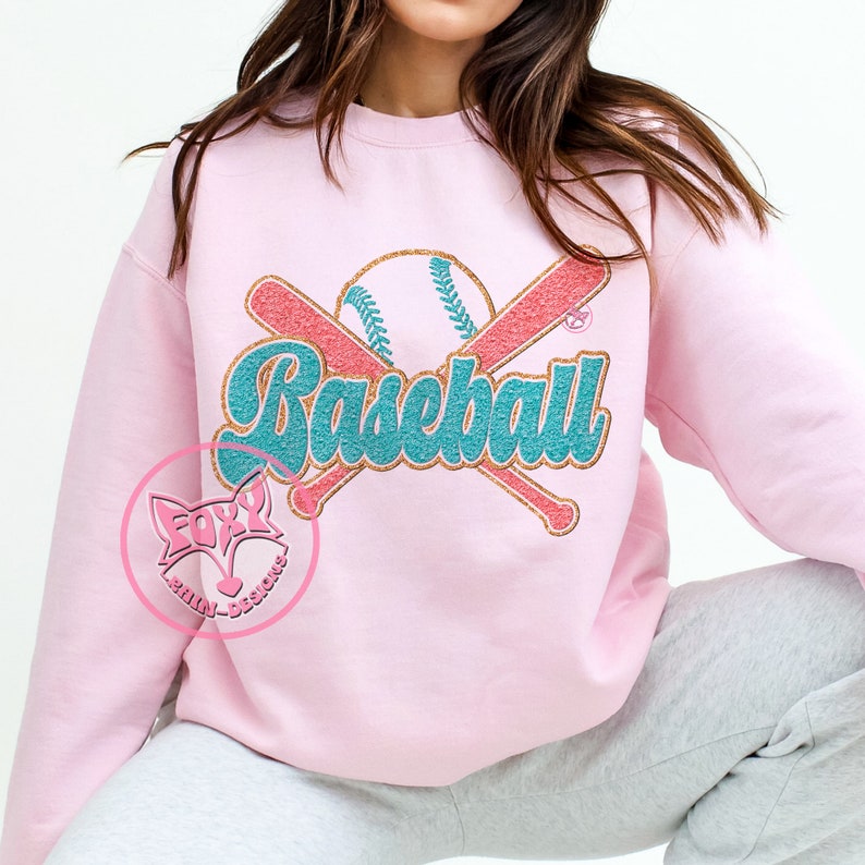 May include: A pink sweatshirt with a graphic design of a baseball, two crossed bats, and the word "Baseball" in a teal and gold font.